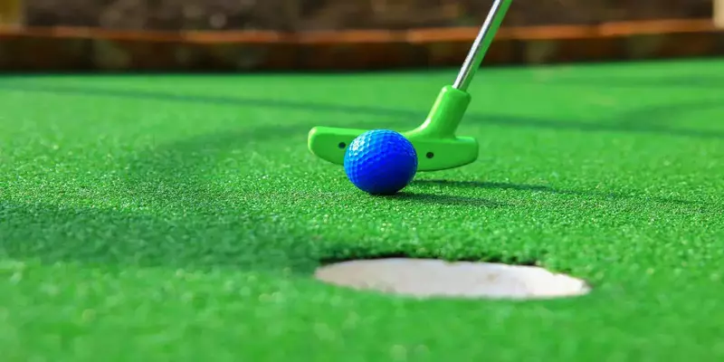 A blue golf ball rolls near hole on mini golf course